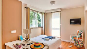 A hotel room with a bed, a desk with a lamp, a chair, a TV, and a window with curtains.