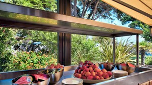 Un buffet proposant une variété de fruits et des plats servis dans des bols, une fenêtre donnant sur un paysage verdoyant et des arbres.