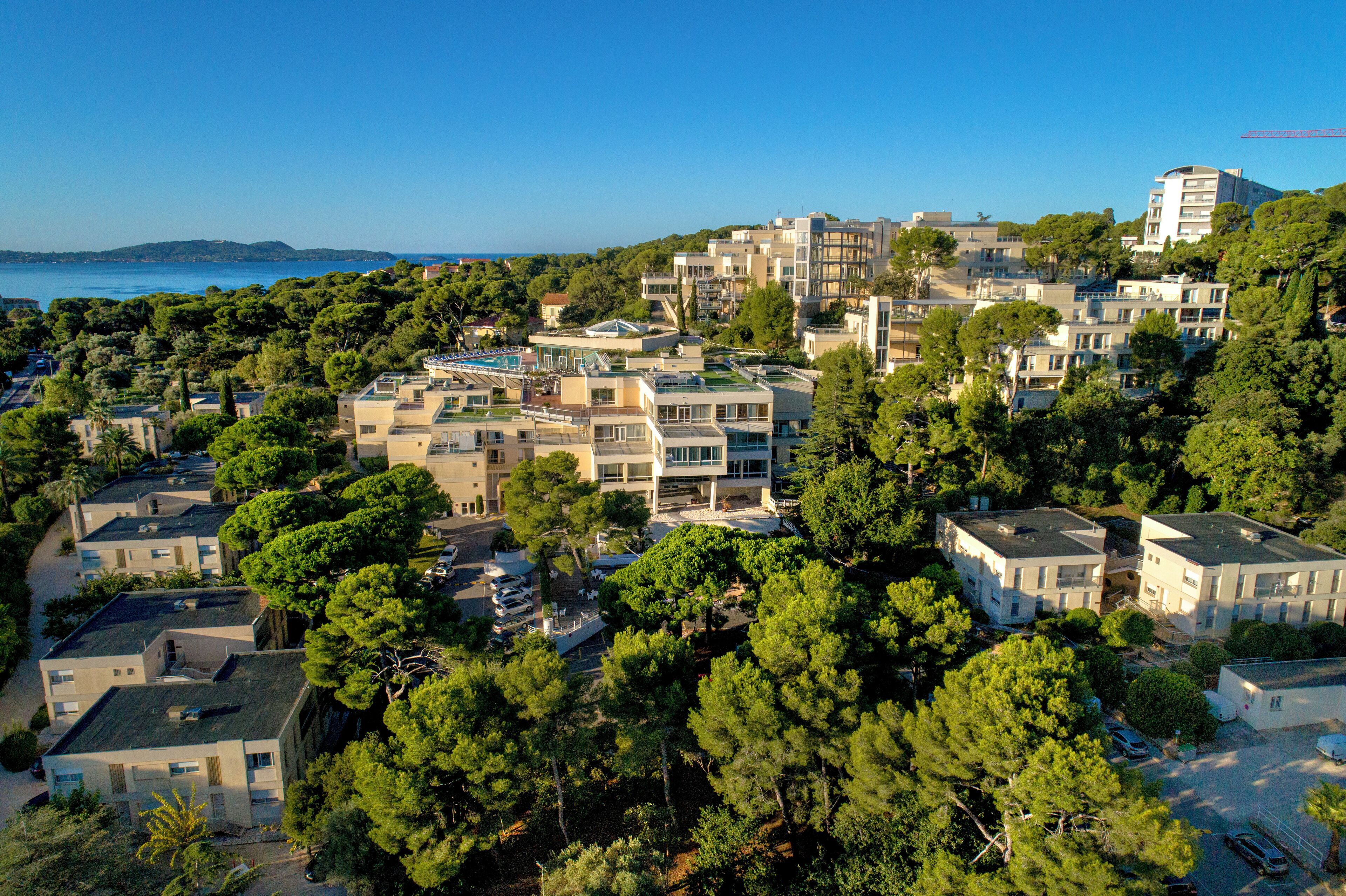 A residential area with modern buildings, dense greenery, and a clear view of the sea.