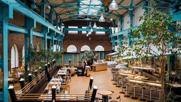 Un restaurante espacioso con techos altos, paredes de ladrillo visto y una zona de bar central.