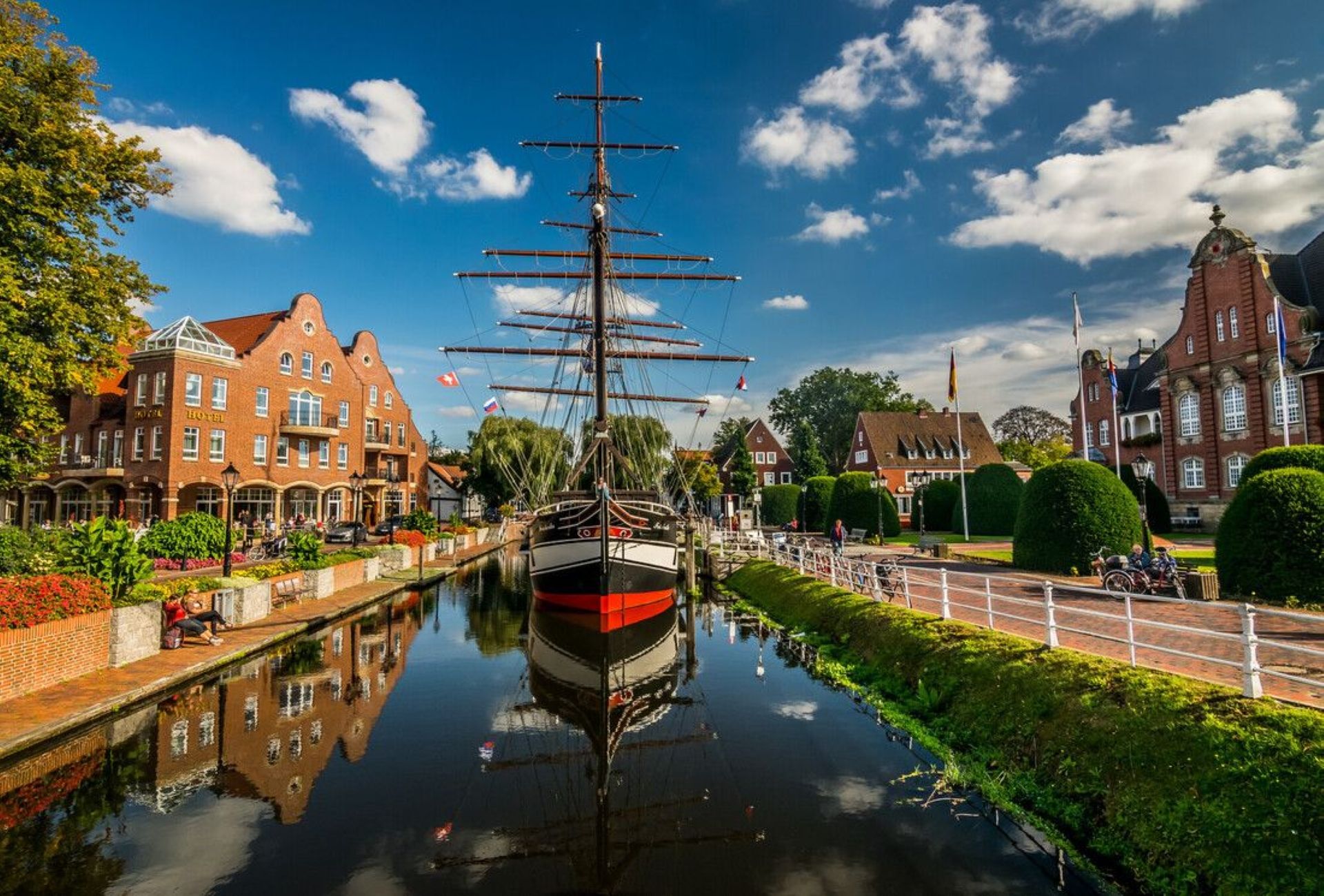 Ein Kanal mit einem hohen Schiff, das an der rechten Seite festgemacht ist, umgeben von historischen Gebäuden und einem Hotel mit roter Fassade.