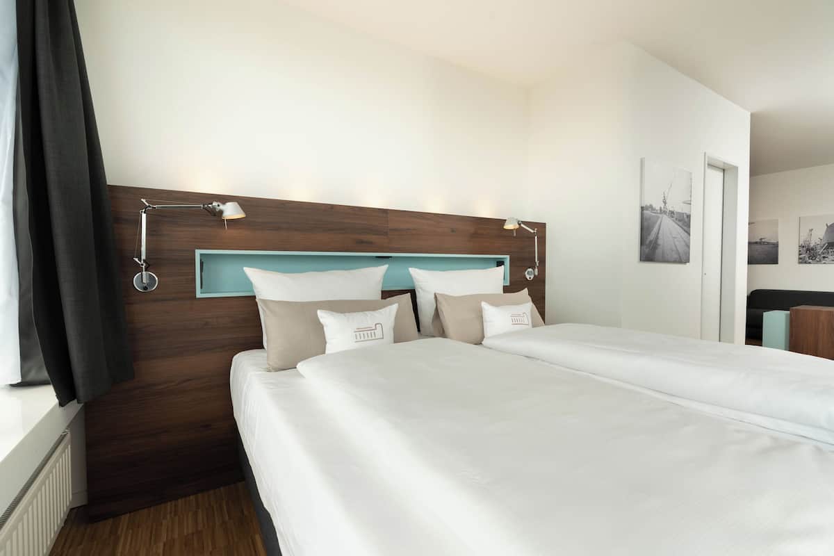 A double bed with a wooden headboard, two bedside lamps, and a window with curtains.