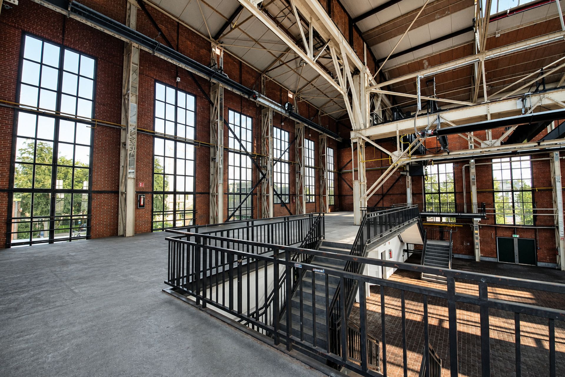 Ein großzügiger, industrieller Innenraum mit hohen Decken, großen Fenstern und einer zentralen Treppe.