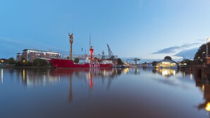 Un puerto tranquilo con un barco rojo llamado 'ELBE' atracado, rodeado de edificios industriales y grúas.