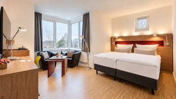 Ein Hotelzimmer mit Bett, einer Couch, einem Schreibtisch und einem fenster mit Vorhängen.