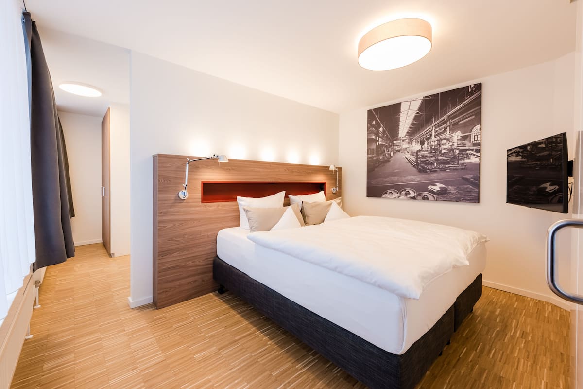 A modern hotel room with a wooden headboard, a large bed with white linens, and two wall-mounted light fixtures.