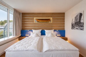 Una habitación de hotel moderna con una cama grande, cabecero de madera y vistas a la ciudad.