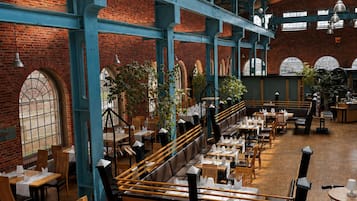 Ein großzügiges Restaurant mit Ziegelwänden, Holztischen und blauen Stahlträgern.