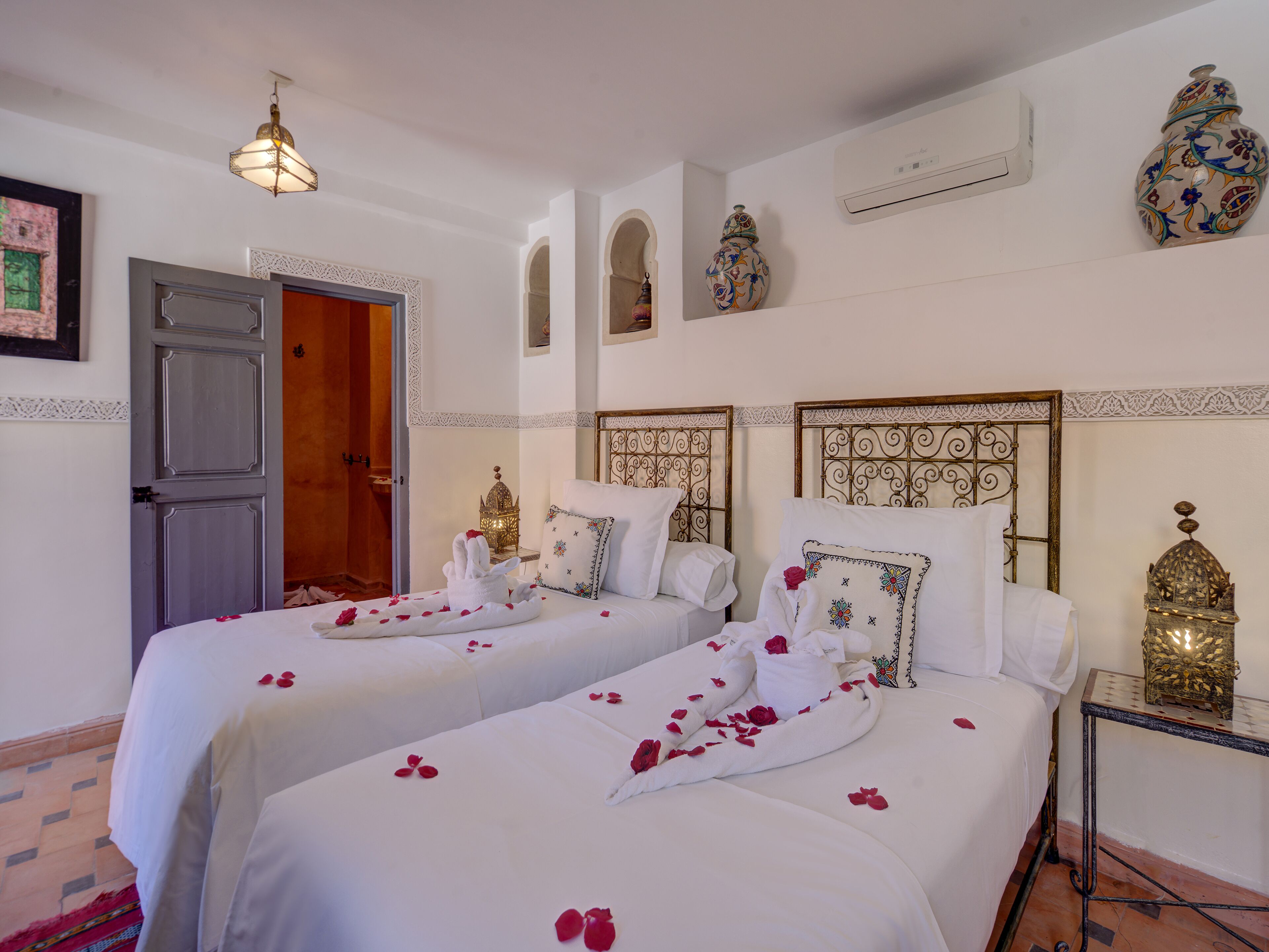 A hotel room with two beds, a nightstand, a decorative lamp, and a door.