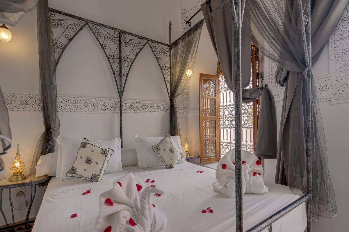 A bed with a canopy, decorative pillows, and rose petals on the bed.