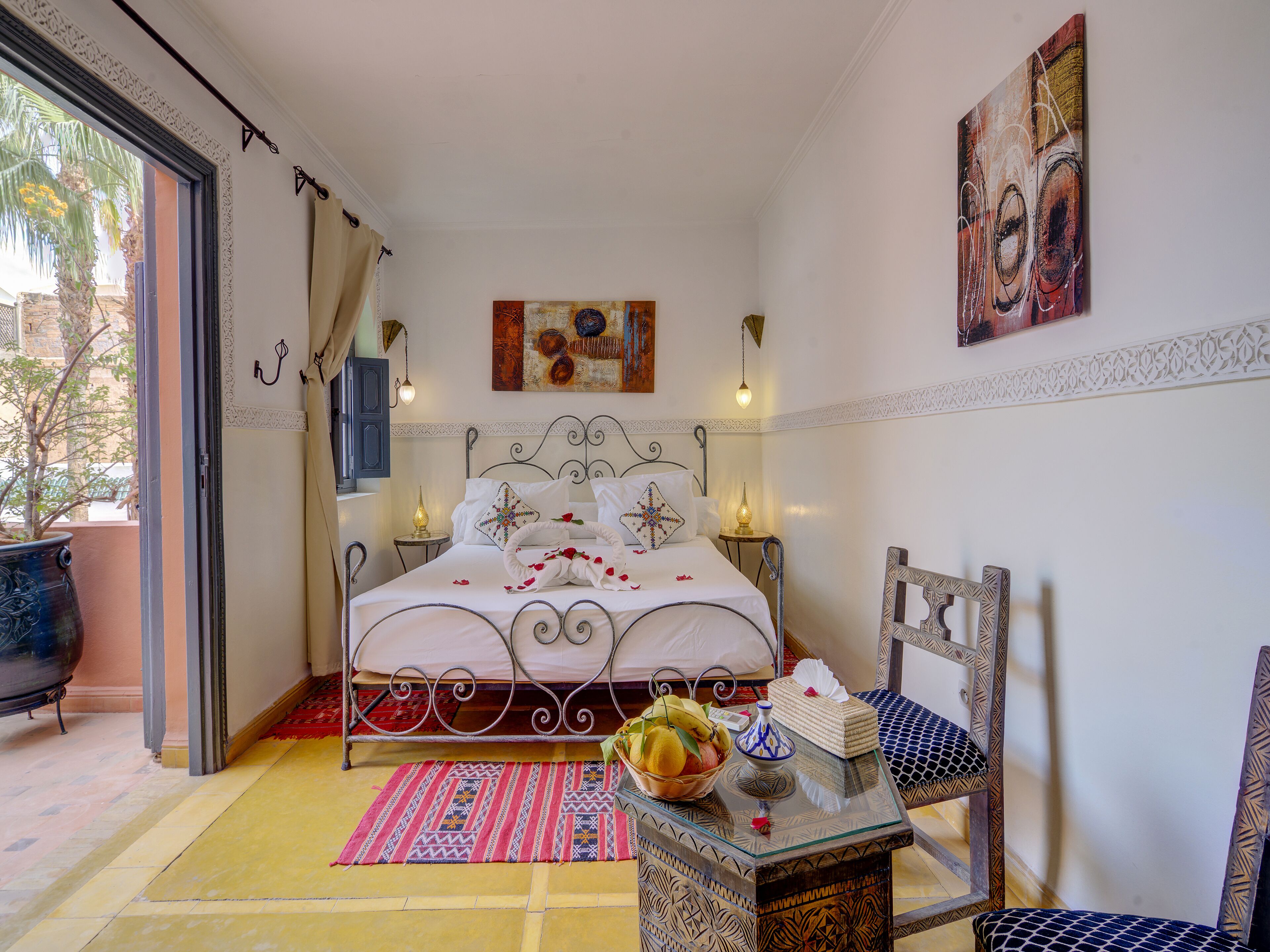 Un dormitorio ordenado con cama, lámparas de noche, un adorno en la pared y una mesita con fruteros.