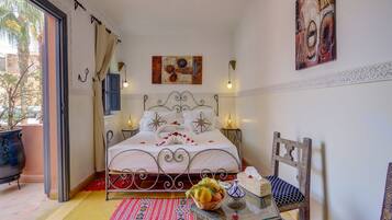 Un dormitorio ordenado con cama, lámparas de noche, un adorno en la pared y una mesita con fruteros.