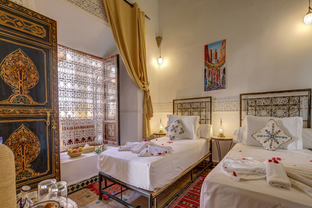 A traditional room with two beds, a decorative door, and a view of a street scene through a window with a curtain.