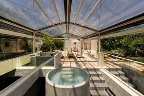 A covered outdoor area with a pool, seating, and a stone wall in the background. - Leonardo Trulli Resort (Locorotondo)