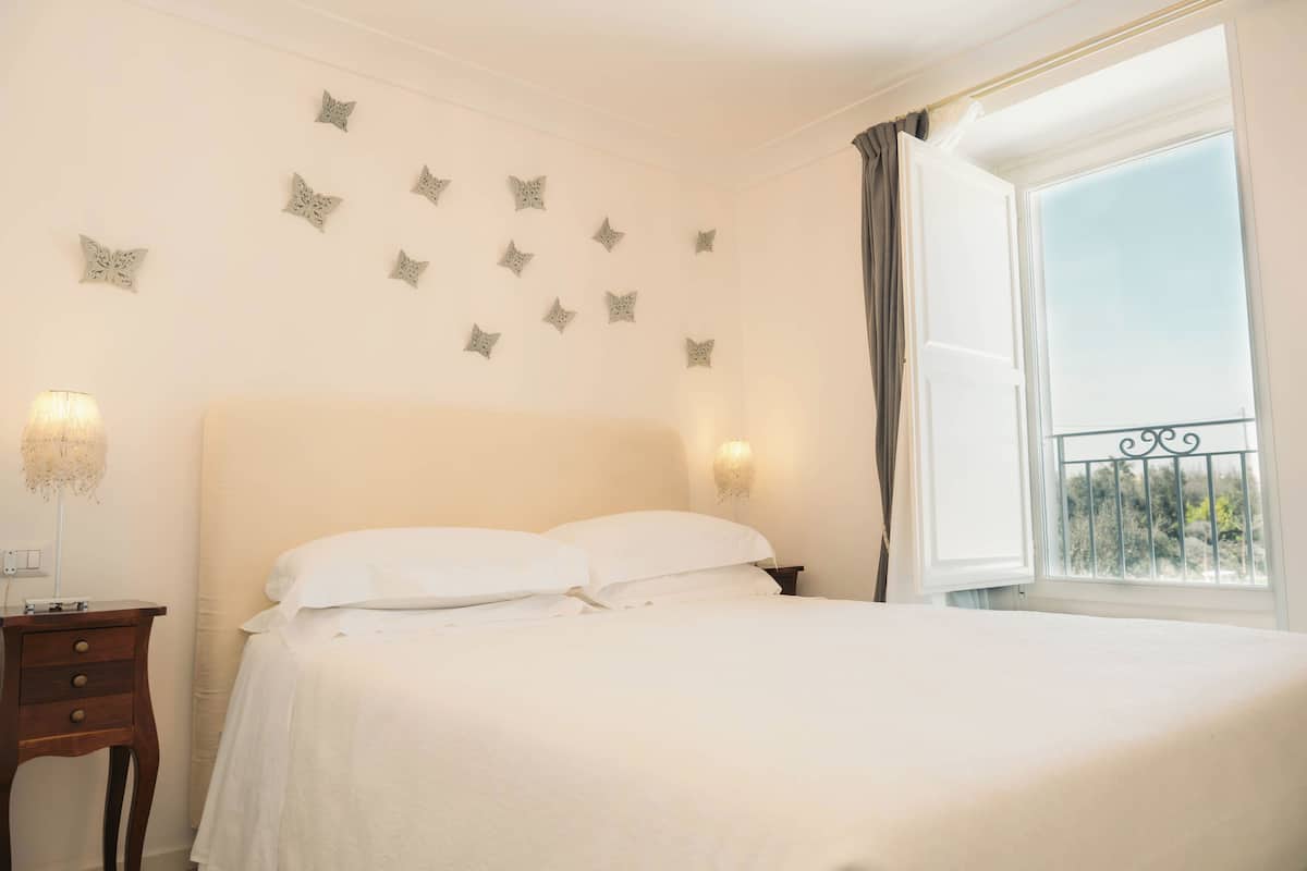 A neatly made bed with white linens, a bedside table with a lamp, and decorative star-shaped wall art.