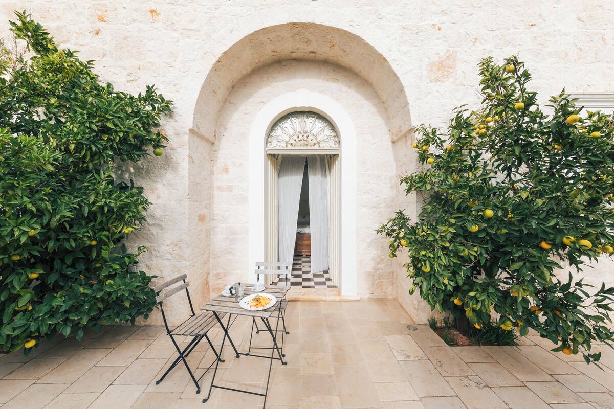 An outdoor patio with a checkered floor, a table with a plate of food, and two lemon trees.