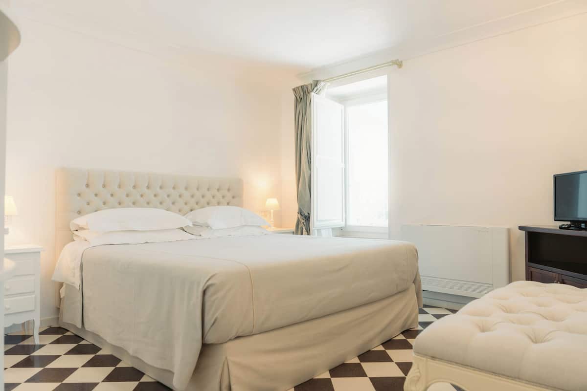 A hotel room with a large bed, a television, a window with curtains, and a radiator.