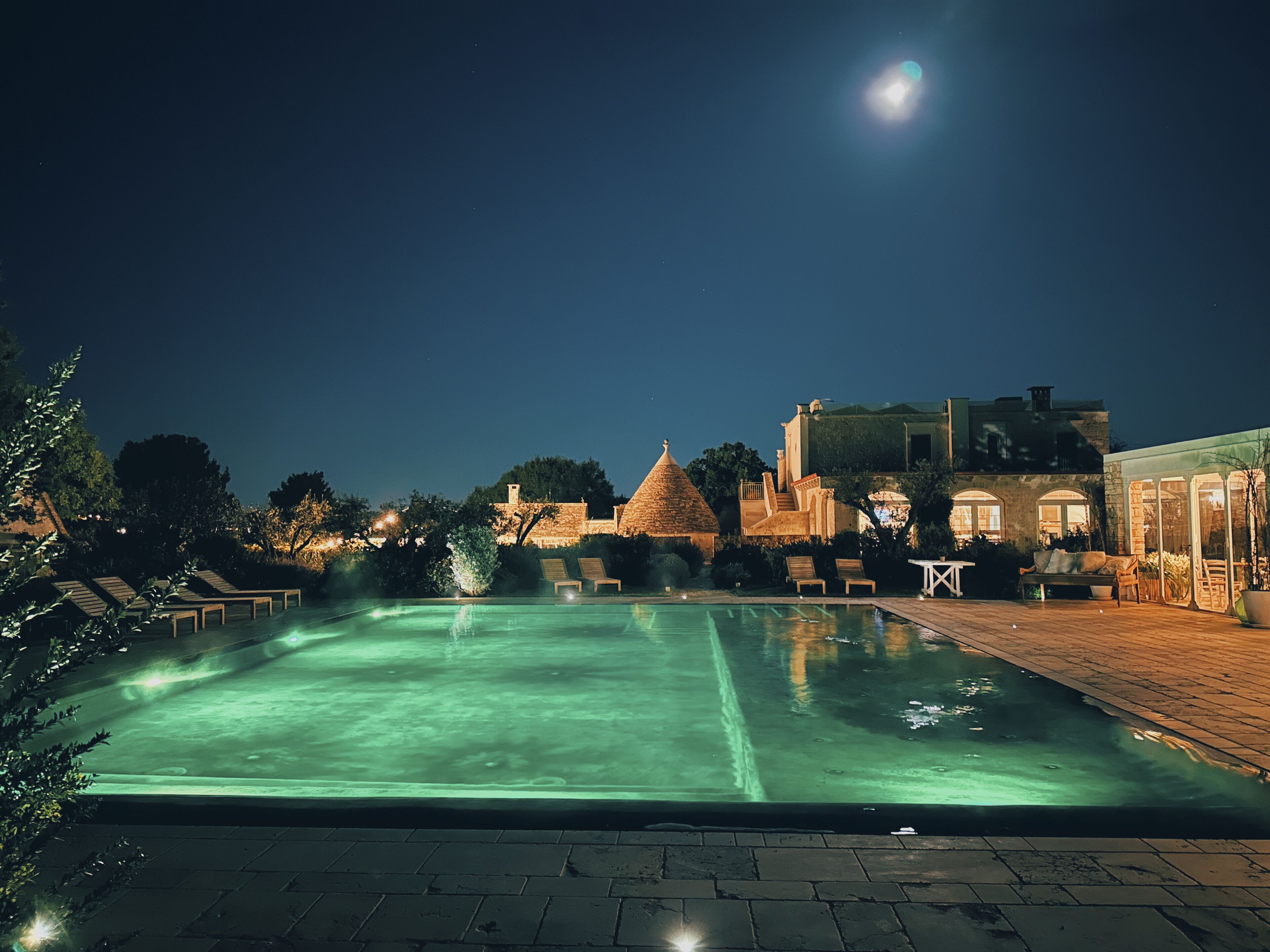 A nighttime swimming pool with lounge chairs and a building in the background. - Leonardo Trulli Resort (Locorotondo)