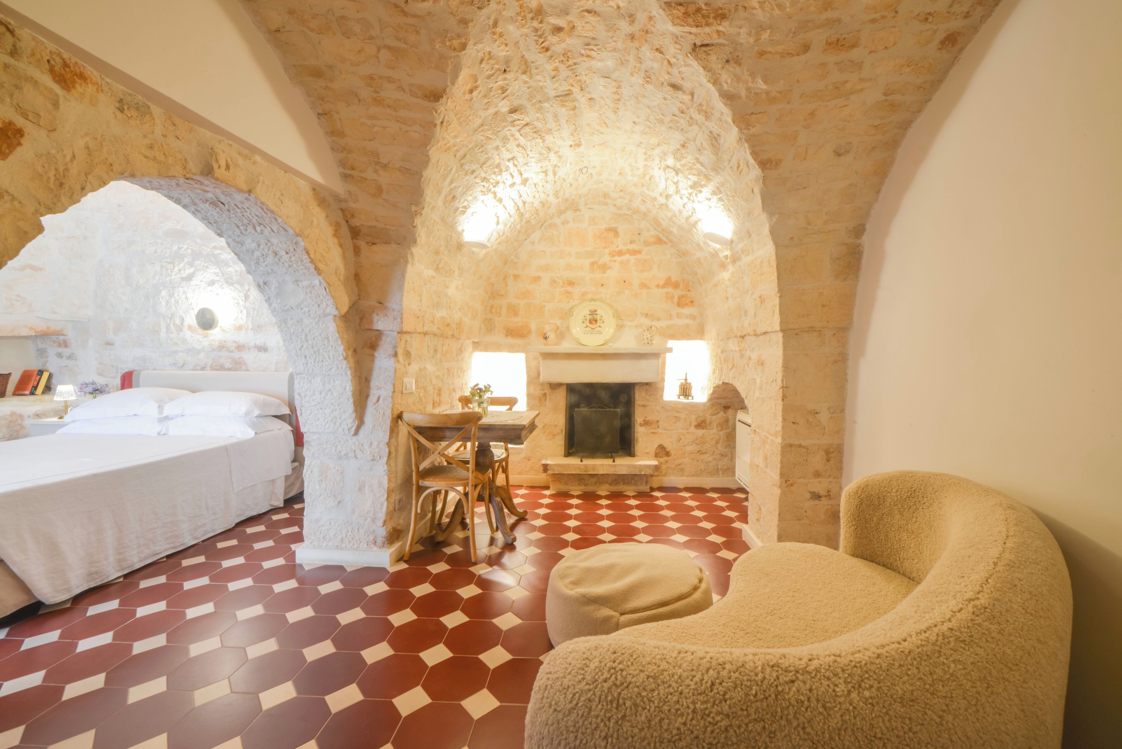 A room with a stone ceiling, a fireplace, a bed, a dining table with chairs, and a red and white checkered floor.