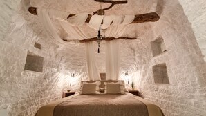 A stone-walled bedroom with a bed, draped white fabric, and a hanging light fixture. - Leonardo Trulli Resort (Locorotondo)