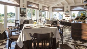 A dining area with checkered flooring, tables set with dinnerware, and large windows offering a view of the outdoors. - Leonardo Trulli Resort (Locorotondo)
