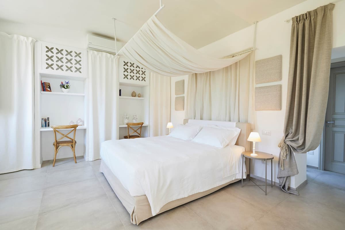 A bedroom with a bed, bedside tables, a chair, a desk, and shelves.