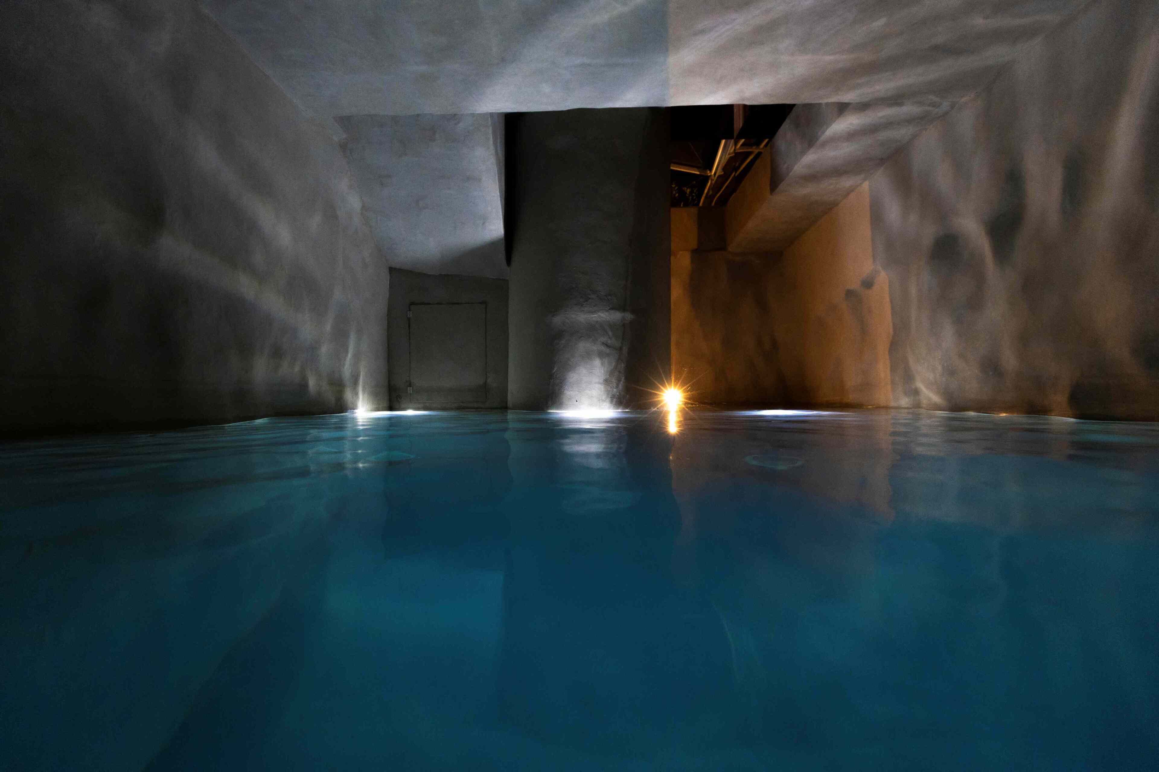 An indoor swimming pool with a clear water surface, walls with a textured pattern, and a single visible door.