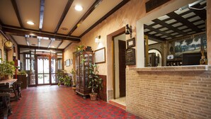 A hotel lobby with a red patterned floor, wooden furniture, and a brick wall.
