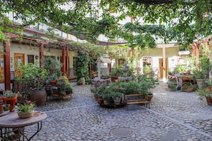 A courtyard with cobblestone flooring, potted plants, and a fountain. - Hostal Castilla (Aranjuez)