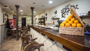 A restaurant interior with a bar area, wooden chairs, a wicker basket of oranges, and a tiled floor.