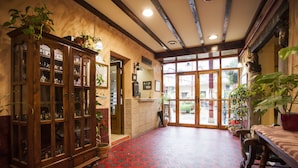 A hallway with a wooden cabinet filled with glassware, a red patterned floor, and a large window with a view of the outside.