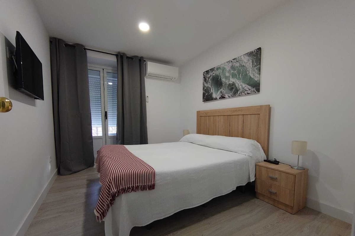 Quarto com cama, mesa de cabeceira, televisão e um quadro na parede.