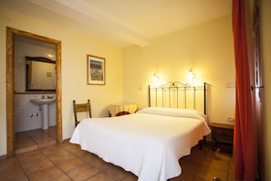 A bedroom with a bed, a bedside table, a lamp, a mirror, and a bathroom with a sink. - Hostal Castilla (Aranjuez)