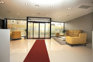 A modern lobby with a red carpet, a yellow sofa, and a glass door entrance.