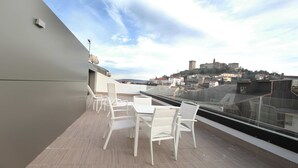 Une terrasse sur le toit, dotée d’une table et de chaises, offrant une vue sur un paysage urbain historique, avec ses bâtiments et une colline.