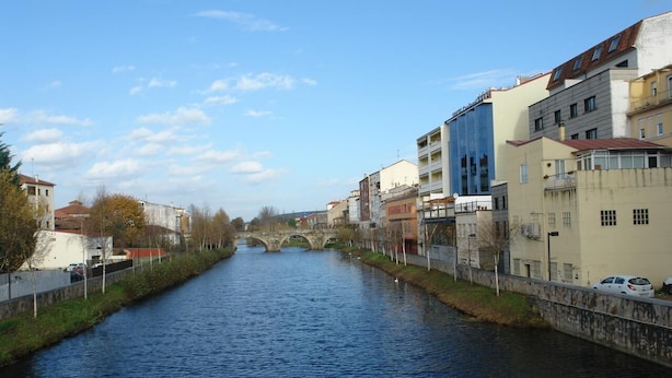Ein Fluss mit einer Steinbrücke in der Ferne, gesäumt von Gebäuden und einem Bürgersteig.