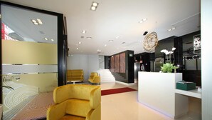Un hall d’hôtel moderne avec un comptoir d’accueil, un fauteuil jaune et un escalier menant à l’étage supérieur.