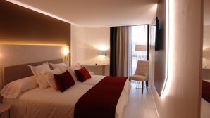 Ein Hotelzimmer mit einem großen Bett, einem Sessel, einem Fernseher und einem Fenster mit Vorhängen.
