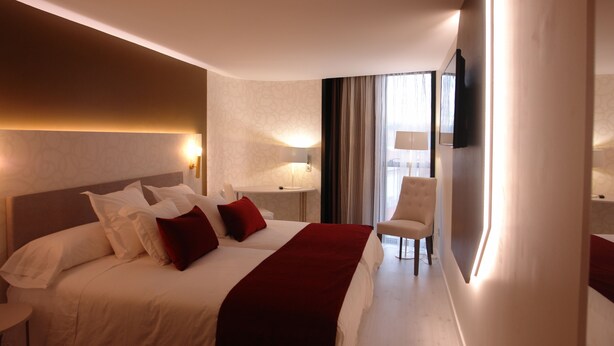 Une chambre d’hôtel avec un grand lit, une chaise, une télévision et une fenêtre avec des rideaux.