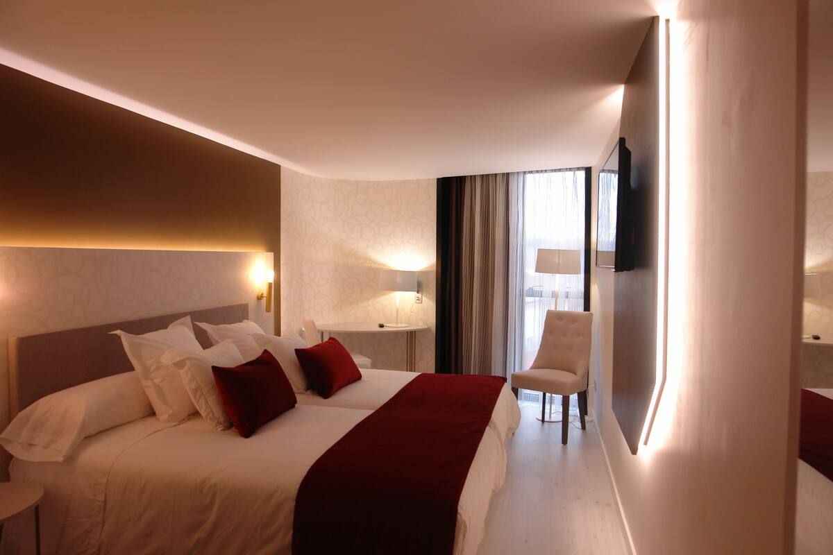 Una habitación de hotel con una cama grande, una silla, un televisor y un ventanal con cortinas.