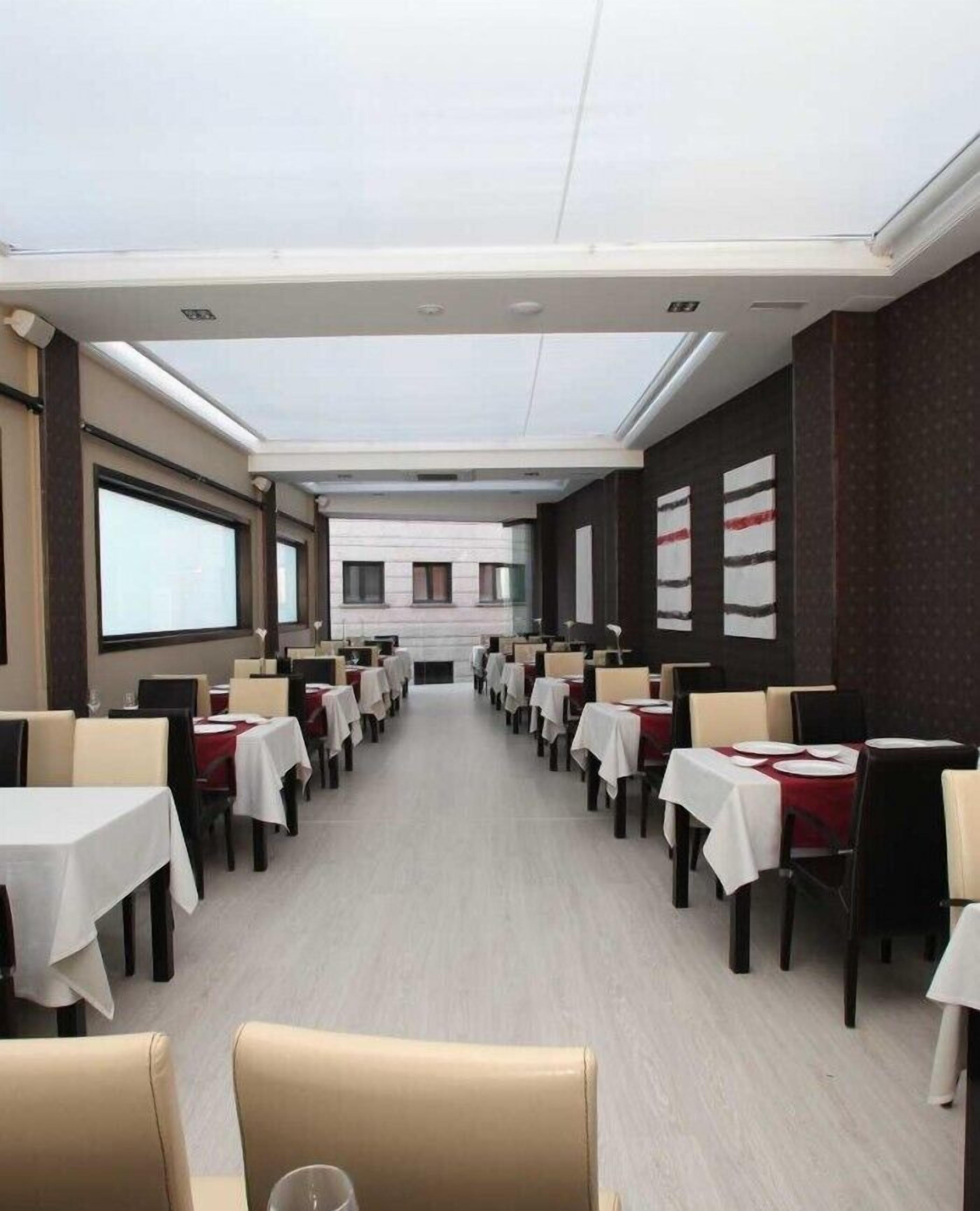 Un comedor amplio con mesas dispuestas para una comida, una pantalla grande al frente y una vista de un edificio en el fondo.