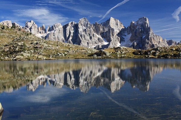 A mountain landscape with rocky terrain and a calm lake reflecting the peaks. - Hotel Stella Alpina (Falcade)