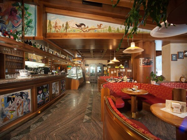 A bar area with wooden decor, a seating area with red upholstered benches, and a mural on the wall depicting wildlife. - Hotel Stella Alpina (Falcade)