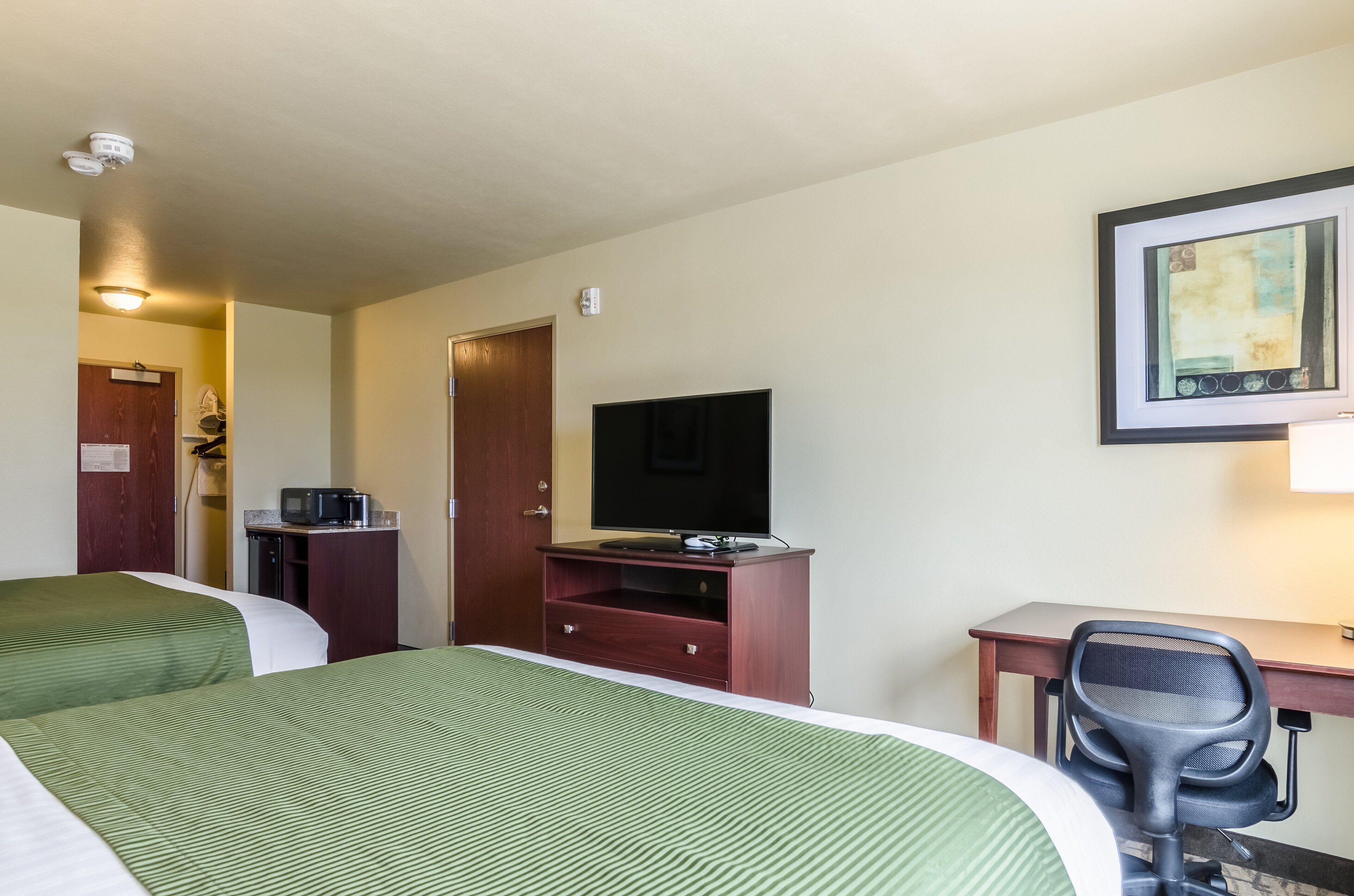 Une chambre d’hôtel avec deux lits, un bureau avec une chaise, une télévision, un four à micro-ondes et une porte donnant sur une autre chambre.