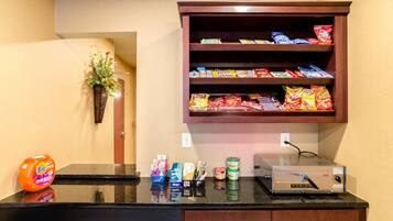 Una kitchenette con microondas, cafetera y estante lleno de bocadillos.