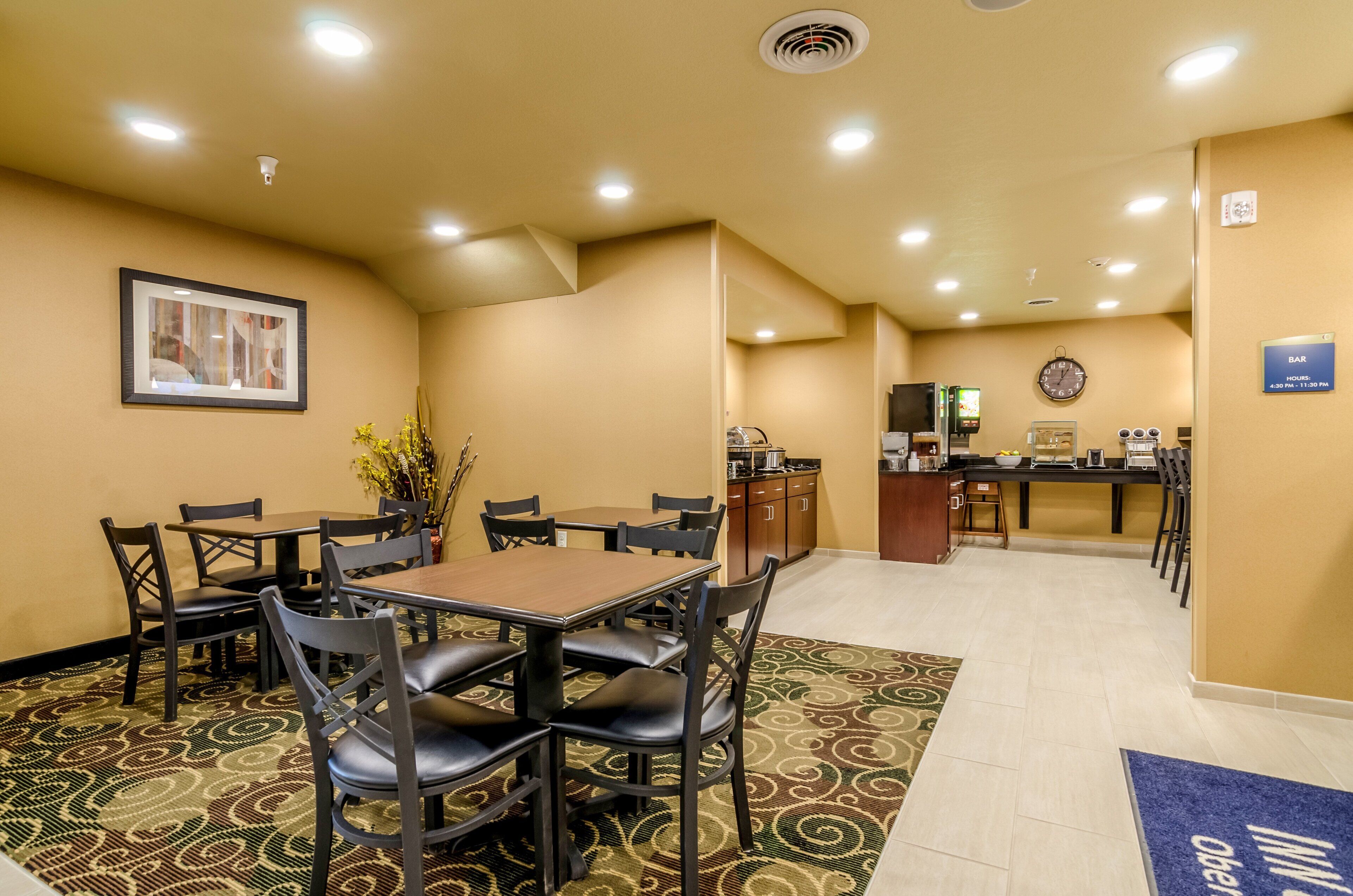 A hotel lobby with a dining area, a reception desk, and a clock on the wall.