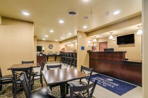 A hotel reception area with a reception desk, a clock, a television, and a dining area with tables and chairs. - Cobblestone Inn & Suites - Oberlin (Oberlin)