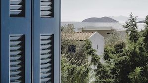 A coastal view with a building featuring a tiled roof and a balcony, surrounded by greenery and overlooking the sea. - Andros Maisonettes (Andros)