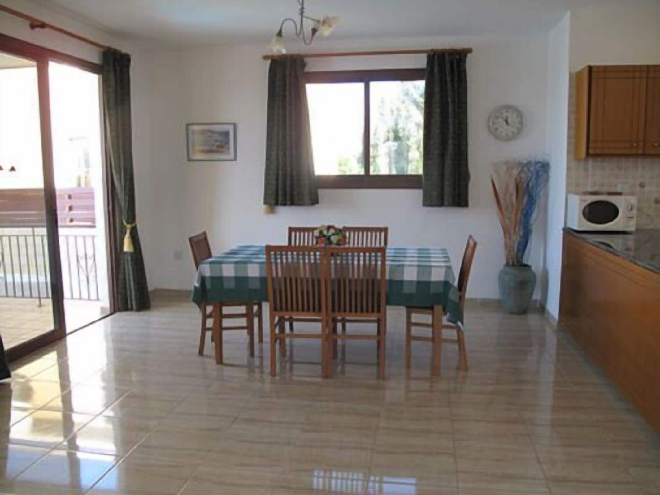 Un comedor con una mesa dispuesta para cuatro, sillas de madera, una ventana con cortinas y un reloj en la pared, con vistas al balcón exterior.