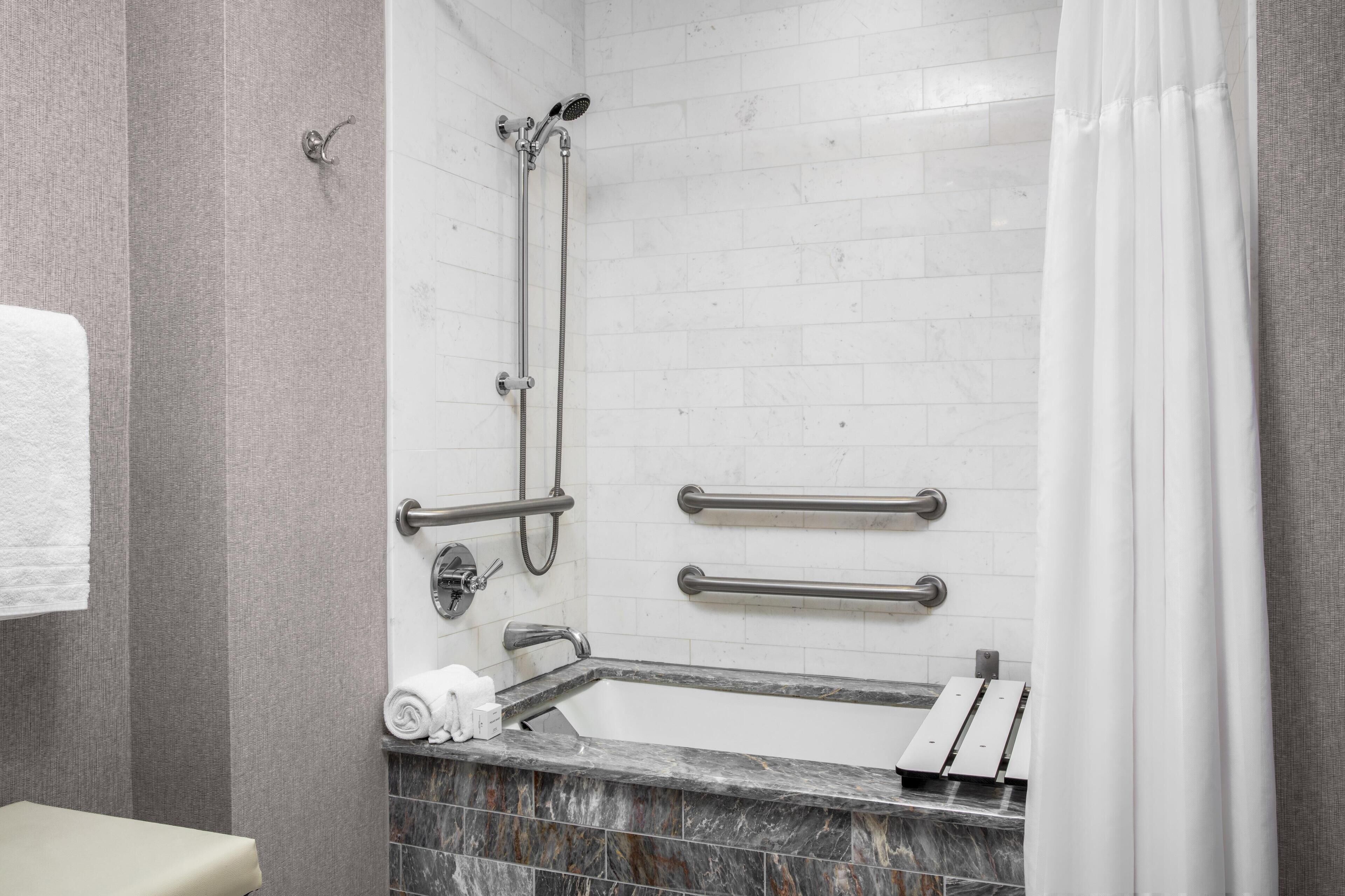 A bathroom with a shower, grab bars, a toilet, and a towel rack.